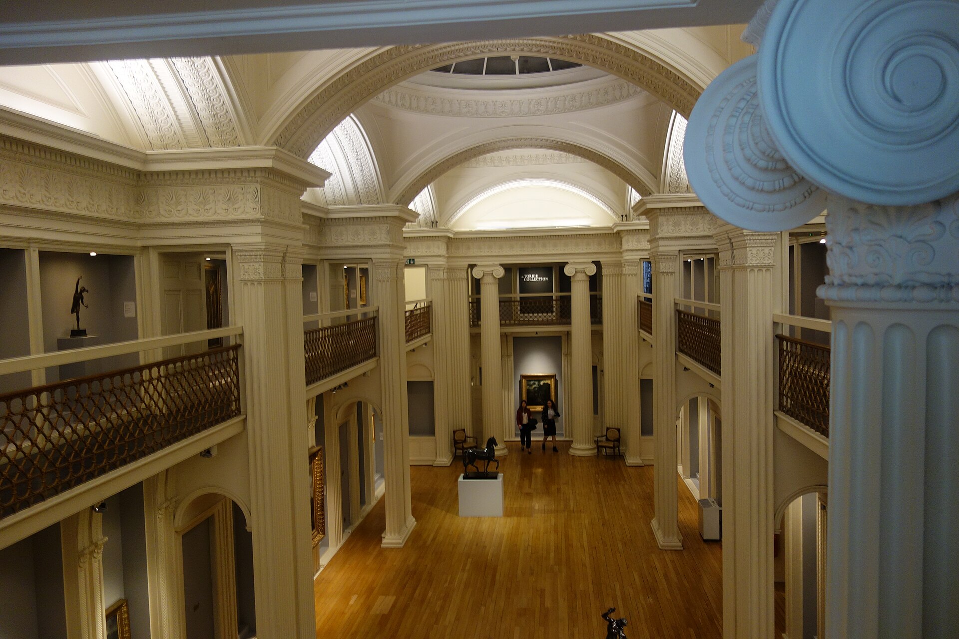 Visitors stand beneath cream arches and an upper balcony inside Talbot Rice Gallery at the University of Edinburgh.