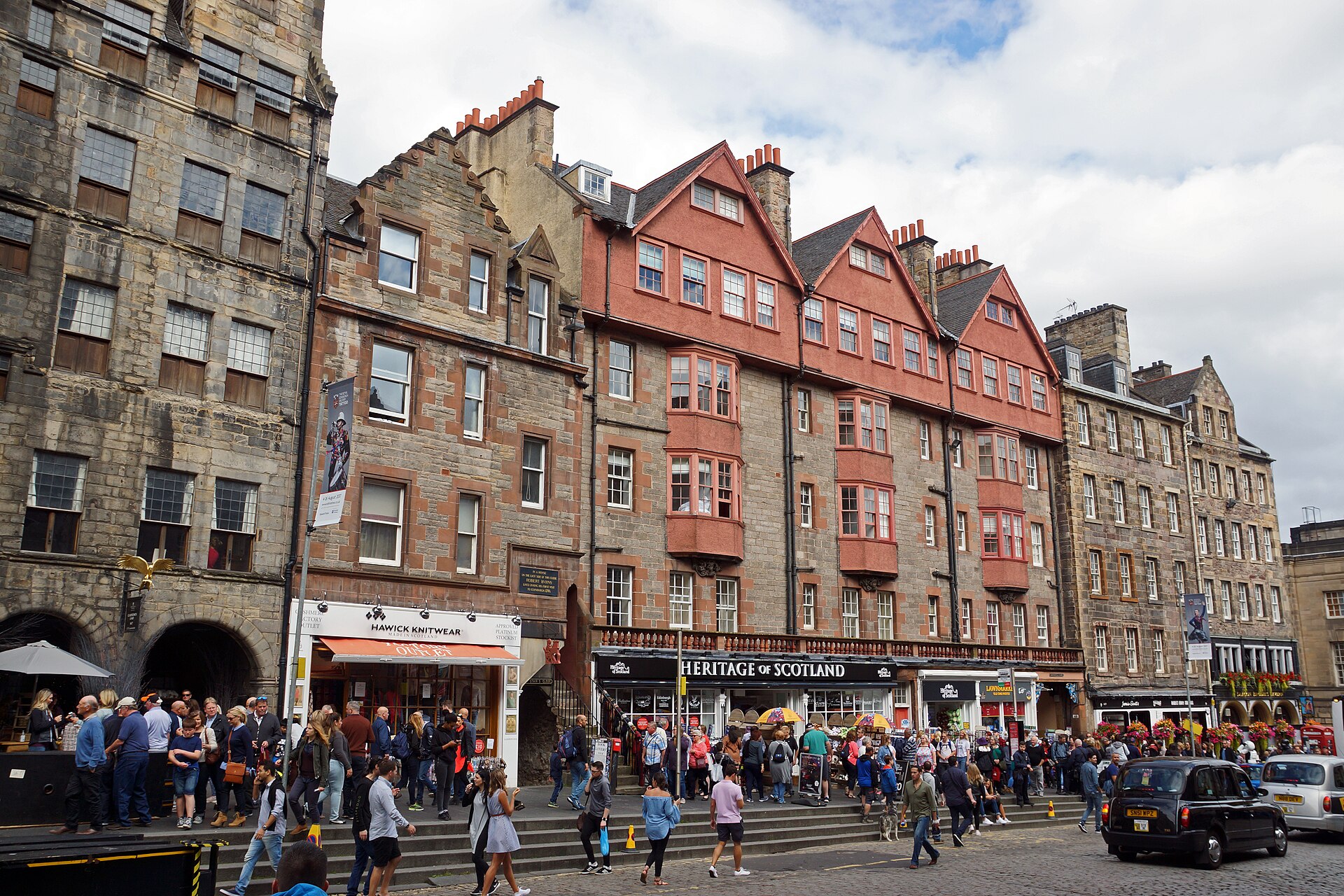Visitors walk past stone tenements and pink gabled buildings along the Lawnmarket section of Edinburgh's Royal Mile.
