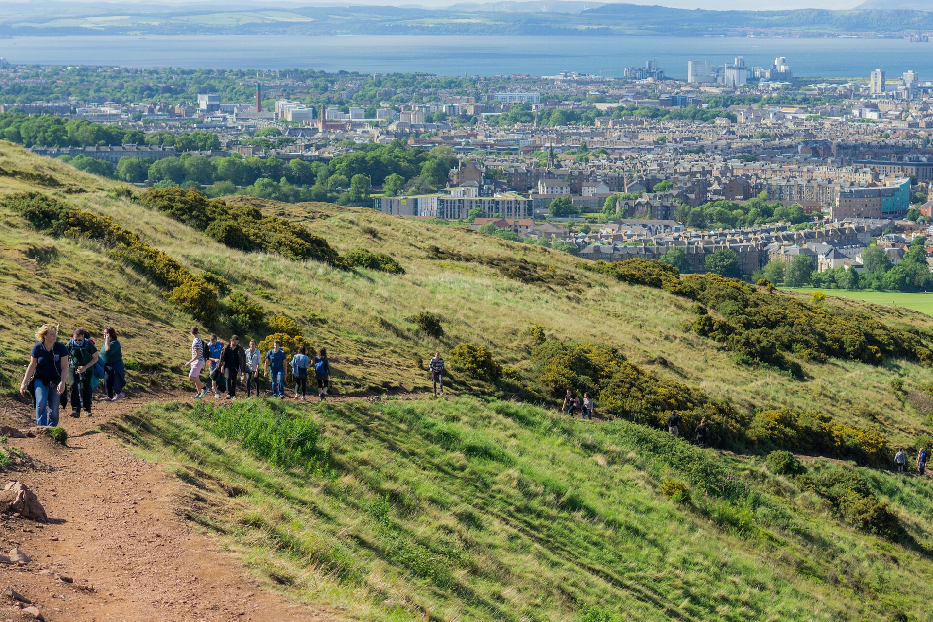 Walkers follow a hillside path on Arthur's Seat, with Edinburgh and the Firth of Forth spread out below.