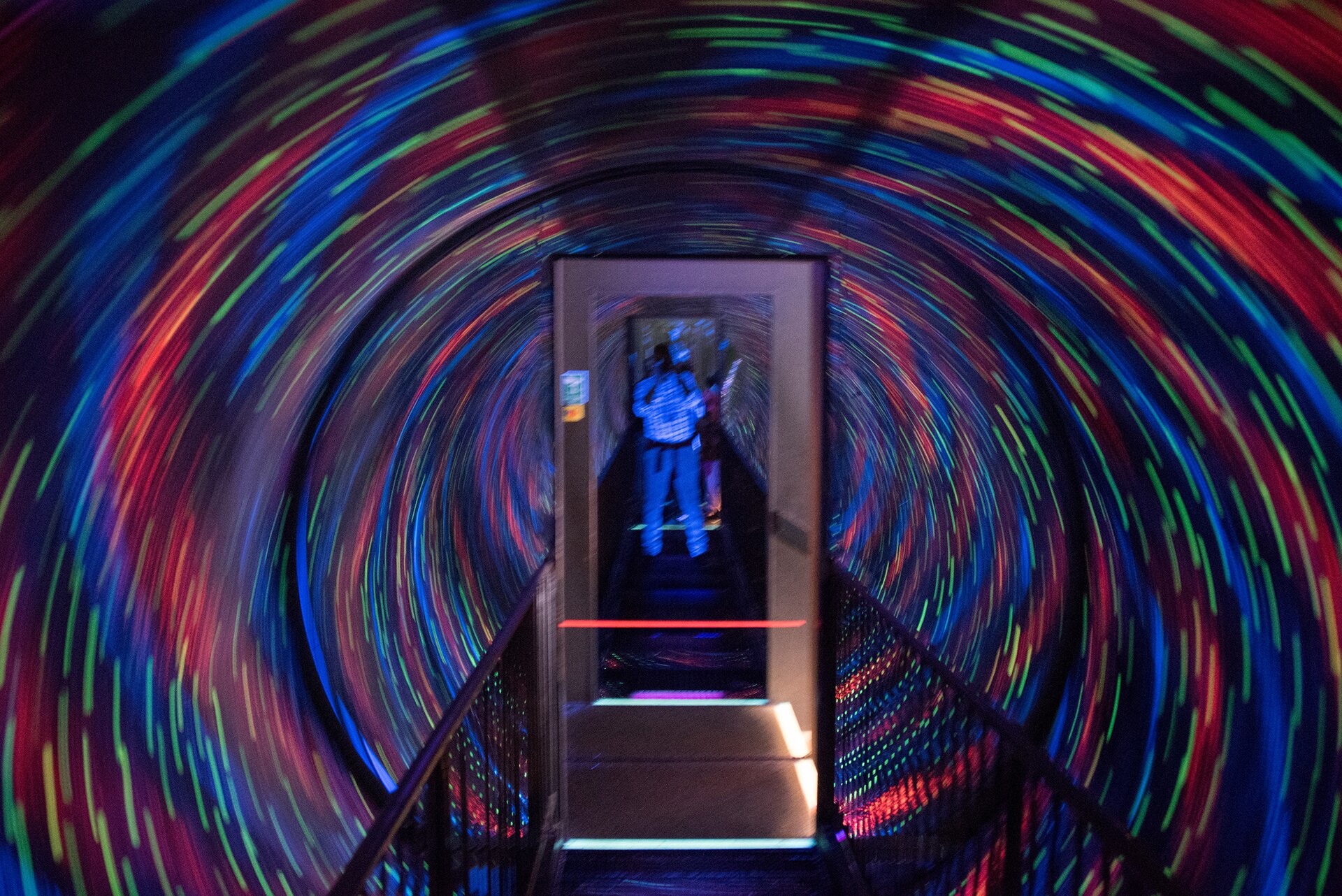 A walkway passes through swirling coloured lights inside Camera Obscura in Edinburgh, with visitors visible at the far end.