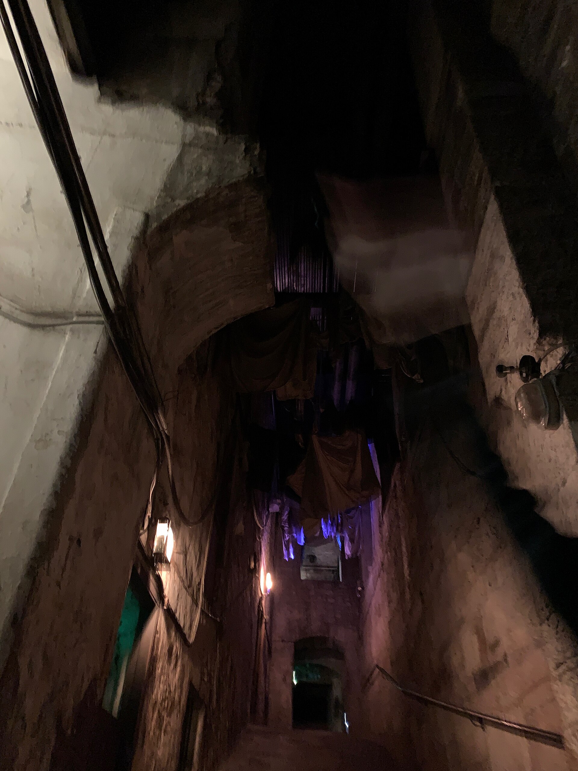 Wall lights illuminate rough masonry and hanging cloth above a narrow underground passage at Mary King's Close in Edinburgh.