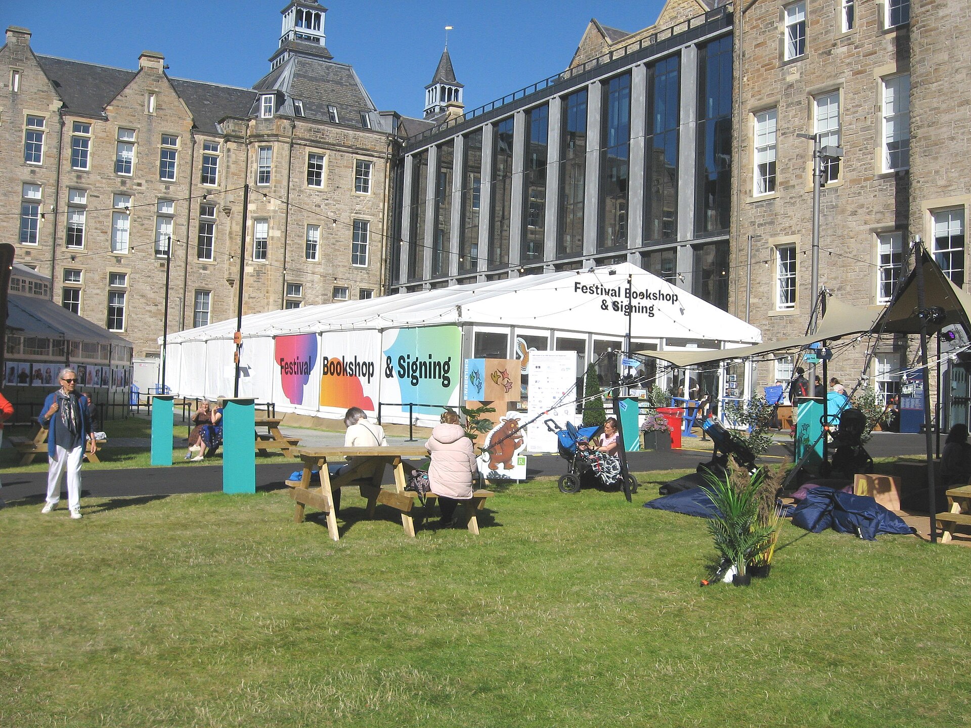 A white Festival Bookshop tent stands beside picnic tables and visitors at Edinburgh's Futures Institute during the 2024 Book Festival.