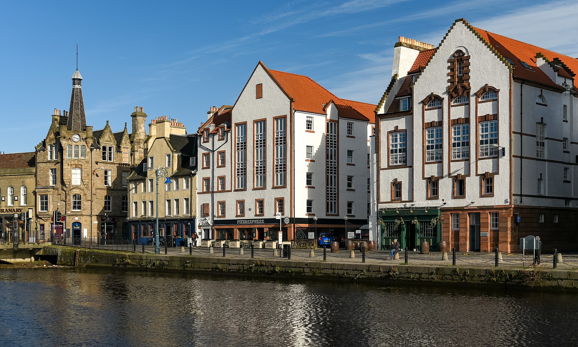 White gabled buildings and a stone clock tower overlook the Water of Leith along Edinburgh's Shore waterfront.